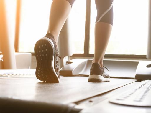 Die Beine einer Frau, die in Sneakers auf einem Laufband läuft.