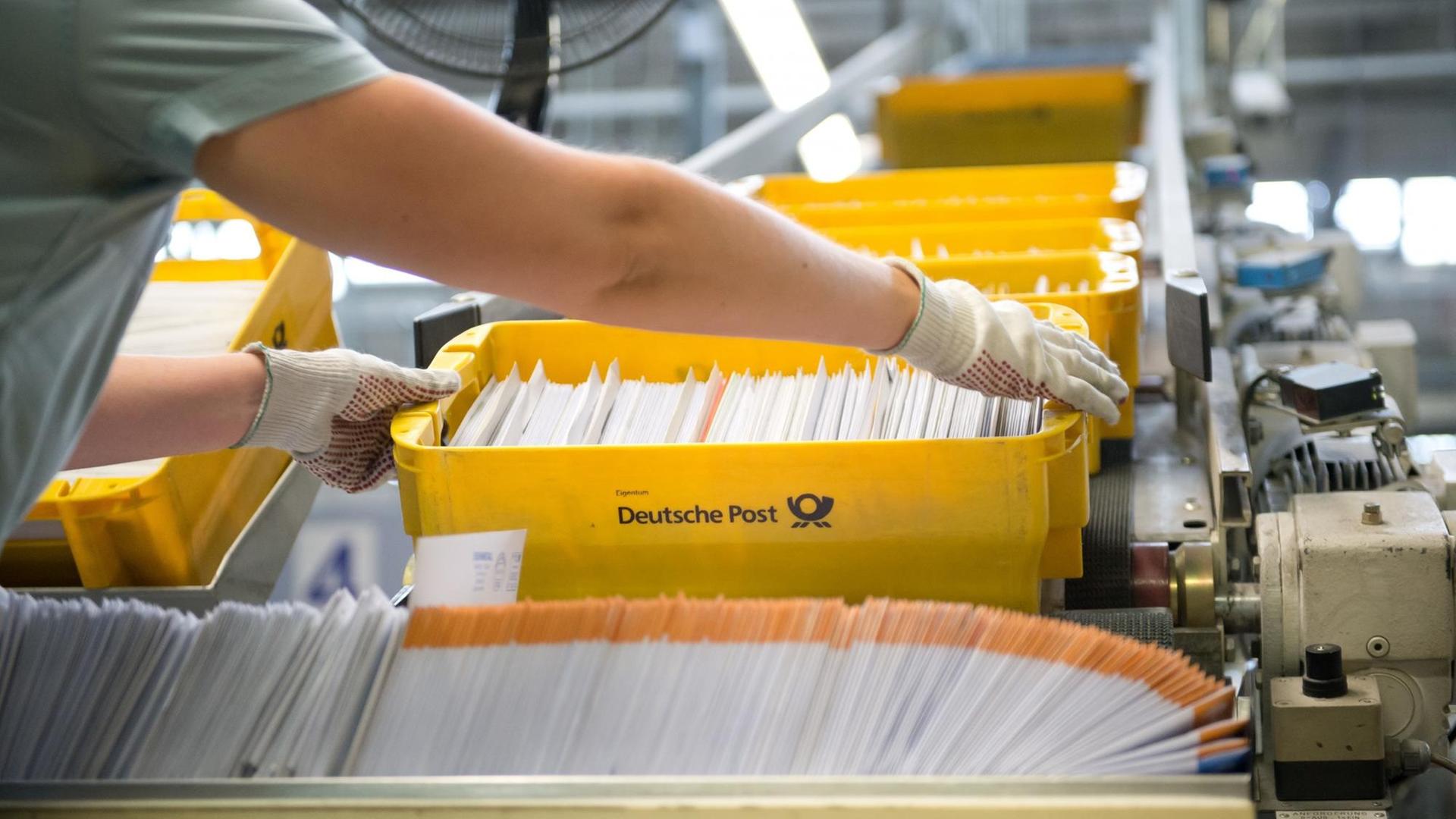 Eine Mitarbeiterin der Deutschen Post nimmt im Briefverteilzentrum in Waiblingen eine Kiste mit Briefen von einem Förderband.