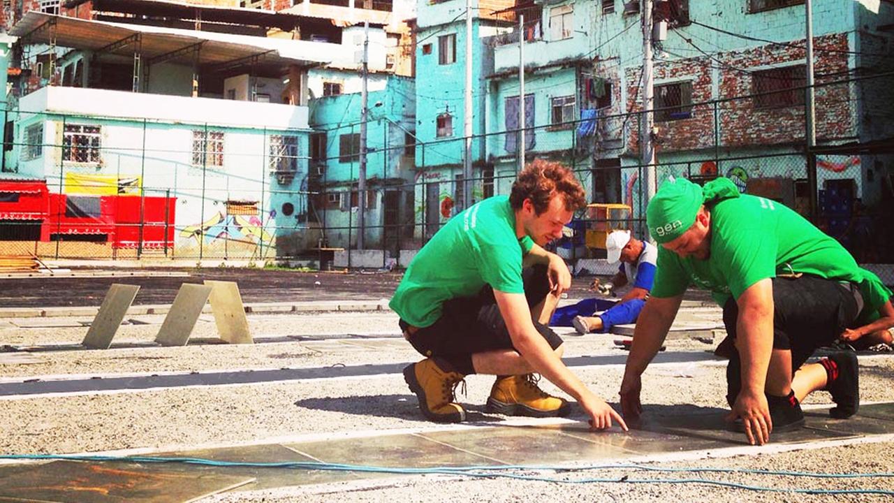 Zwei Männer in grünen T-Shirts verlegen Kinetik-Platten auf einem Fußballplatz in Rio de Janeiro verlegt
