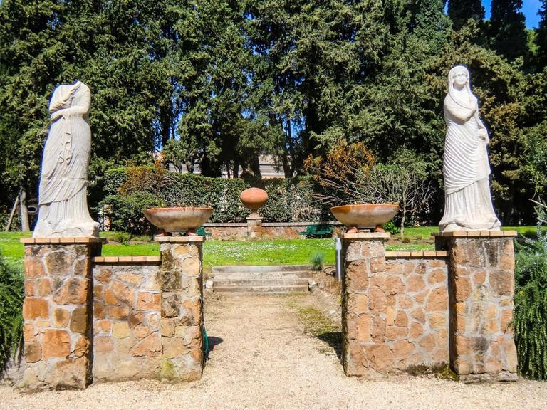 Blick in einen Teil des Gartens der Villa Massimo, der mit zwei nur teilweise erhaltenen, weißen Frauen-Marmorfiguren geschmückt ist.