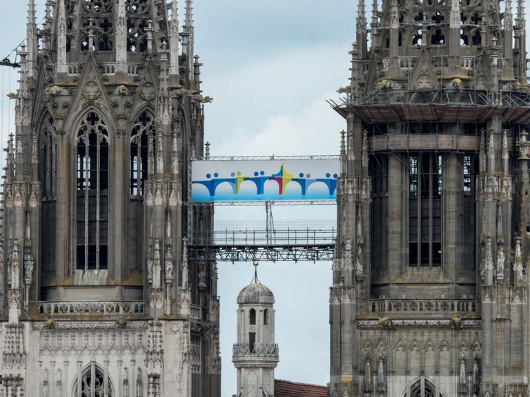 Ein Plakat mit dem Logo des Katholikentages hängt am 27.05.2014 zwischen den Türmen des Doms St. Peter in Regensburg (Bayern).