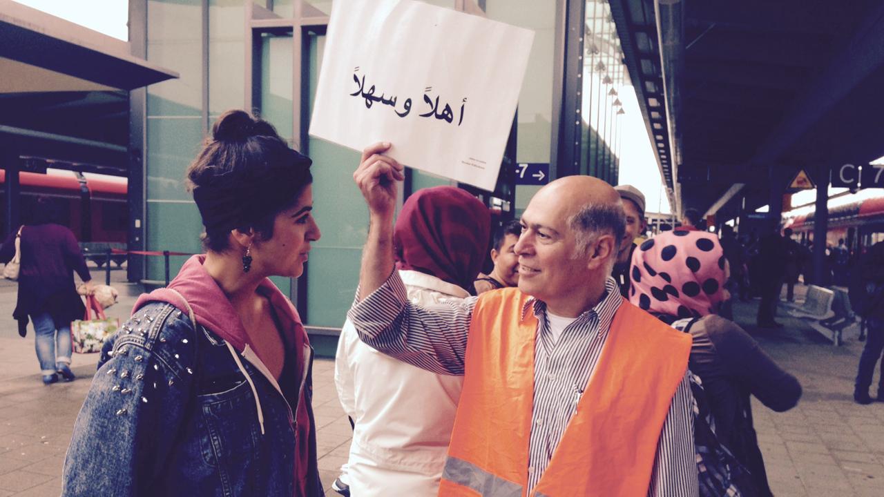Dr. Hikmat Al-Sabty begrüßt am Rostocker Bahnhof ankommende Flüchtlinge mit einem Willkommensschild.