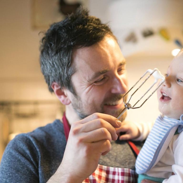 Ein lachender Vater mit kleinem Kind auf dem Arm in der Küche.