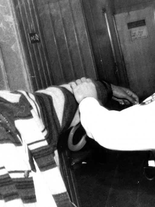 Der Rapper Tupac Shakur 1993 bei einem Termin am Kriminalgericht im New Yorker Stadtteil Manhatten. Tupac guckt in die Kamere und streckt ihr seinen Mittelfinger entgegen. Ein Polizist versucht ihm Handschellen anzulegen.
