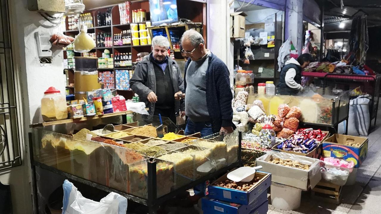 Auf einem Basar im Frühjahr 2019 in der nordsyrischen Stadt Dêrik. Zwei Männer stehen vor einem Geschäft, wo Gewürze und andere Lebensmittelverkauft werden.