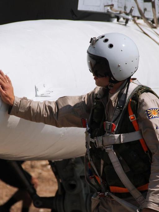 Ein russischer Pilot vor einem Einsatz in Syrien. Er trägt einen Helm und lehnt am Flugzeug.