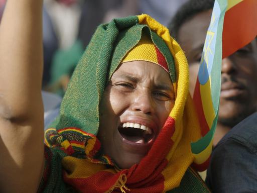 Eine junge Frau hat ein Tuch in den äthiopischen Nationalfarben um den Kopf geschlungen und reckt den Arm in die Höhe.