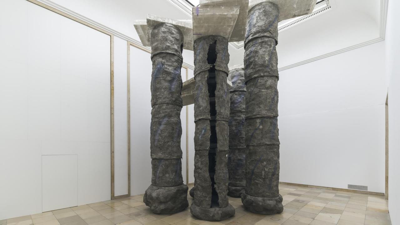 Installationsansicht der Skulptur-Ausstellung von Phyllida Barlow im Haus der Kunst in München. Hier stehen hohle Metallsäulen, auf denen oben Betonplatten balacieren.