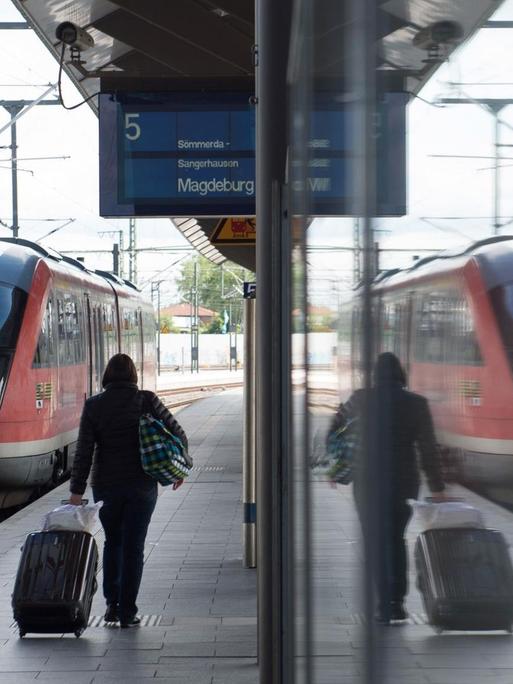 Eine Frau geht am 19.05.2015 am Hauptbahnhof in Erfurt (Thüringen) auf einem Bahnsteig entlang und spiegelt sich in einer Scheibe.