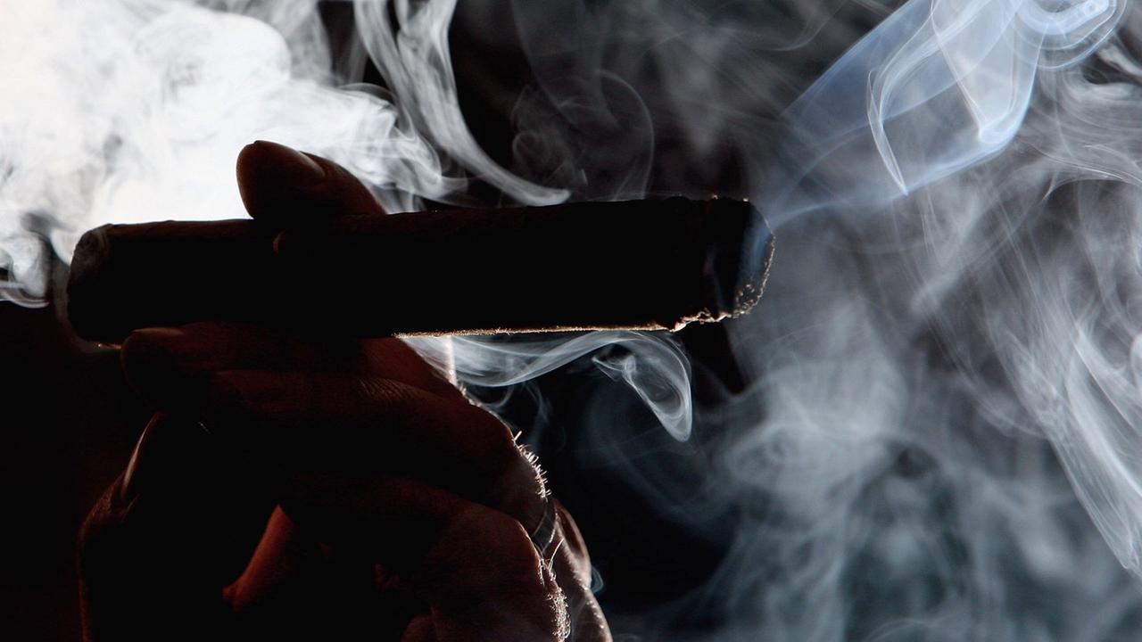 Vom Rauch umwaberte Schattenkontur einer Hand, die eine Zigarre hält.