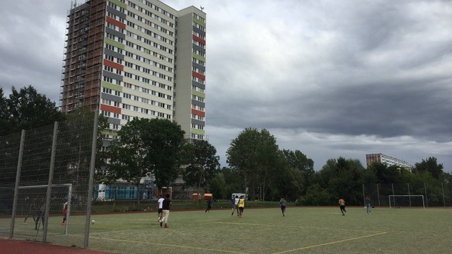 Ein Fußballplatz am Fuße eines Hochhauses. Auf dem Platz trainieren Spieler.