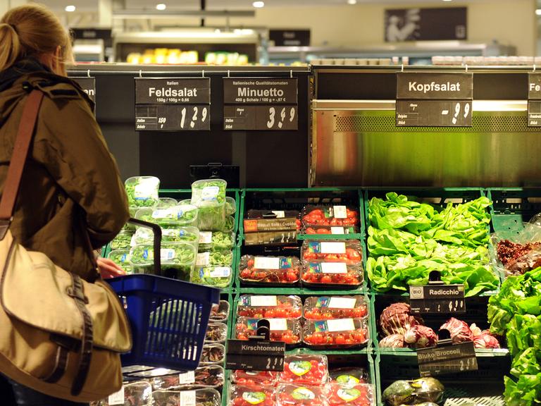 Ein Kundin steht in einem Supermarkt vor einer Auslage mit Salat.
