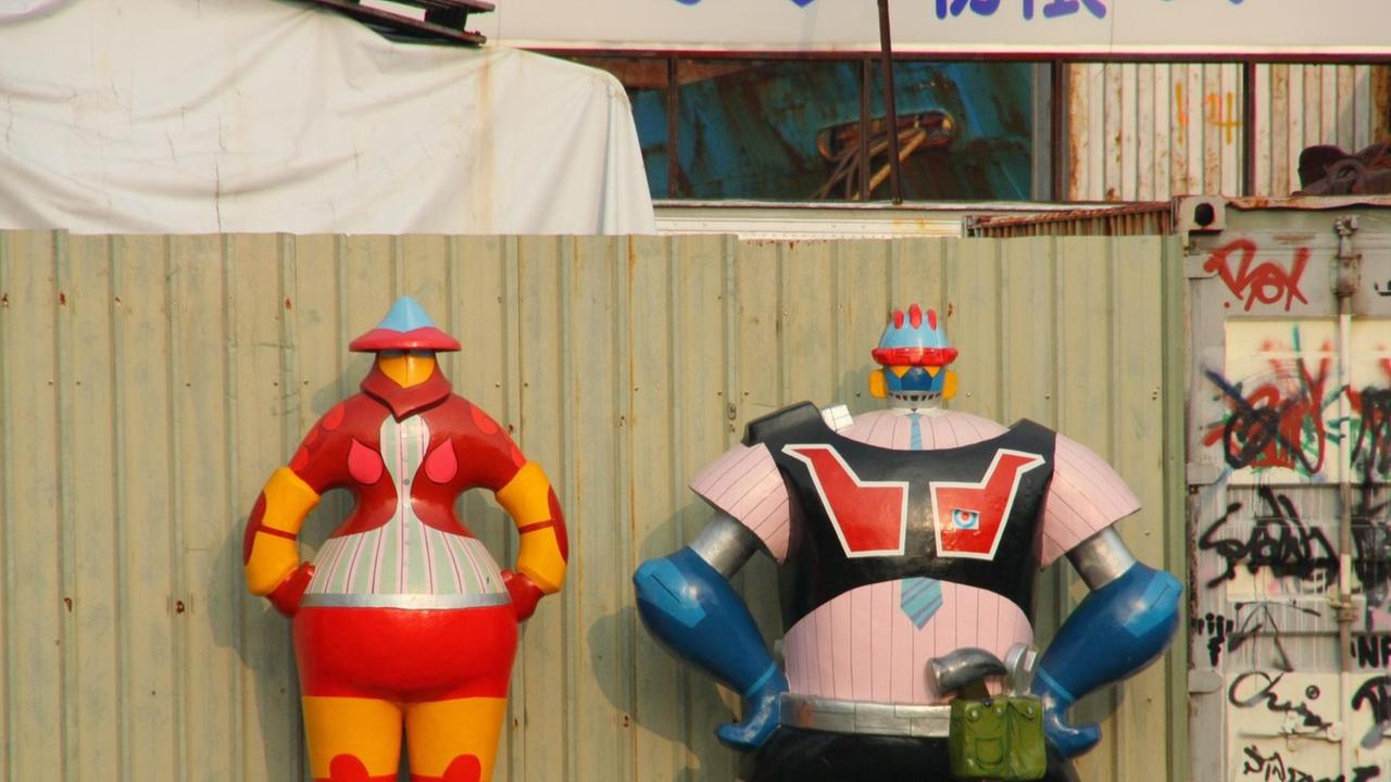 Zwei Roboter-Skulpturen stehen vor einer Baustelle.