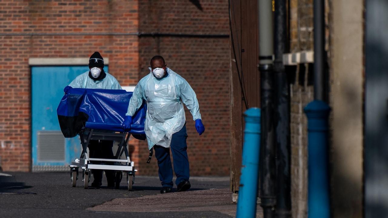 Zwei Krankenhausmitarbeiter des Lewisham-Krankenhauses in London schieben in Schutzkleidung einen Wagen, der für den Transport von Leichen verwendet wird, zur provisorischen Leichenhalle. Das Krankenhaus hat dafür einen Kühlcontainer auf seinem Parkplatz aufgestellt.