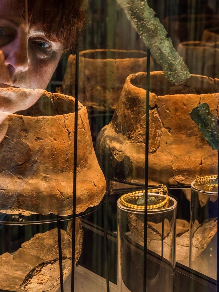 Museumsleiterin Heike Pilz schaut in eine Vitrine mit Grabausstattungen aus der Zeit zwischen 1300 - 1100 v. Chr., die am 04.10.2017 in der neuen Ausstellung "Blutiges Gold - Macht und Gewalt in der Bronzezeit" im Museumsgebäude des Archäologischen Freilichtmuseums Groß Raden (Mecklenburg-Vorpommern) in der Nähe von Sternberg zu sehen sind.