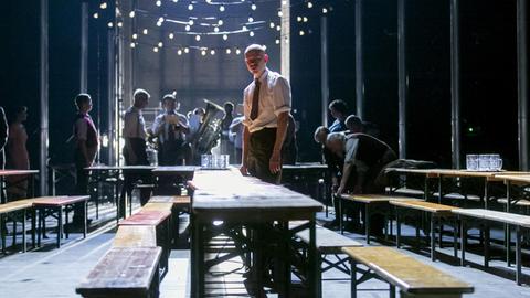 Der Schauspieler Peer Oscar Musinowski steht einsam an einem Biertisch, im Hintergrund spielt ein Blasmusikensemble