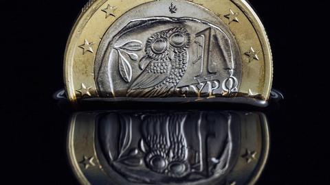 Die griechische Euro-Münze versinkt in schwarzer Flüssigkeit.