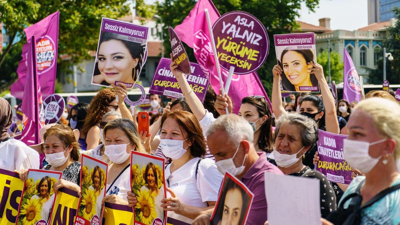 Viele dicht beieinander stehende Menschen mit Mundschutz demonstrieren mit lila Plakaten und rosa Fahnen sowie mit Fotos getöteter Frauen gegen Gewalt gegen Frauen.