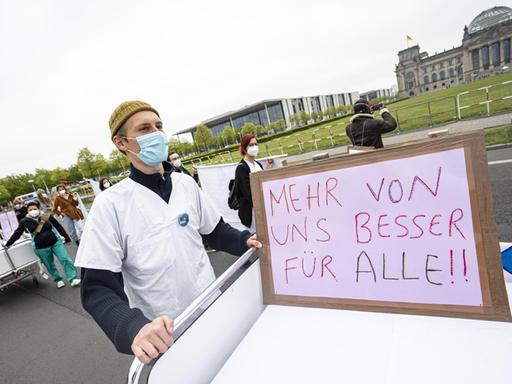 Ein Teilnehmer der Aktion «Der Pflege geht die Luft aus» der Bundespflegekammer und des Berliner Walk of Care geht mit einem Krankenhausbett und einem Schild mit der Aufschrift "Mehr von uns besser für alle" am Reichstagsgebäude vorbei