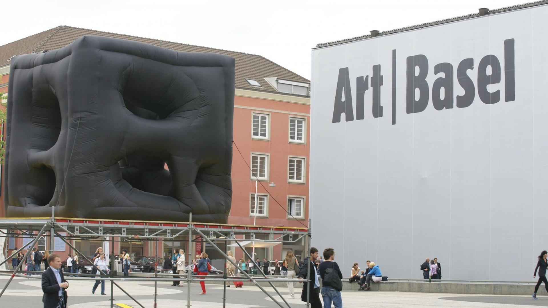 Vor der Messehalle der Art Basel steht eine große, schwarze, viereckige Skulptur. 