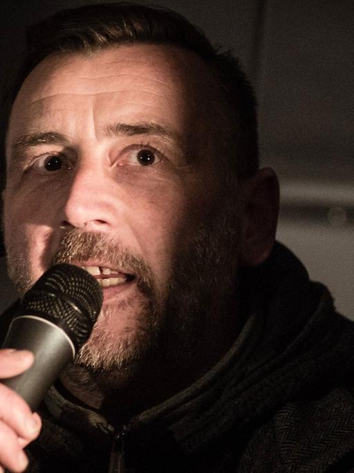 Pegida-Mitbegründer Lutz Bachmann in spärlichem Licht mit Mikrofon in der Hand.