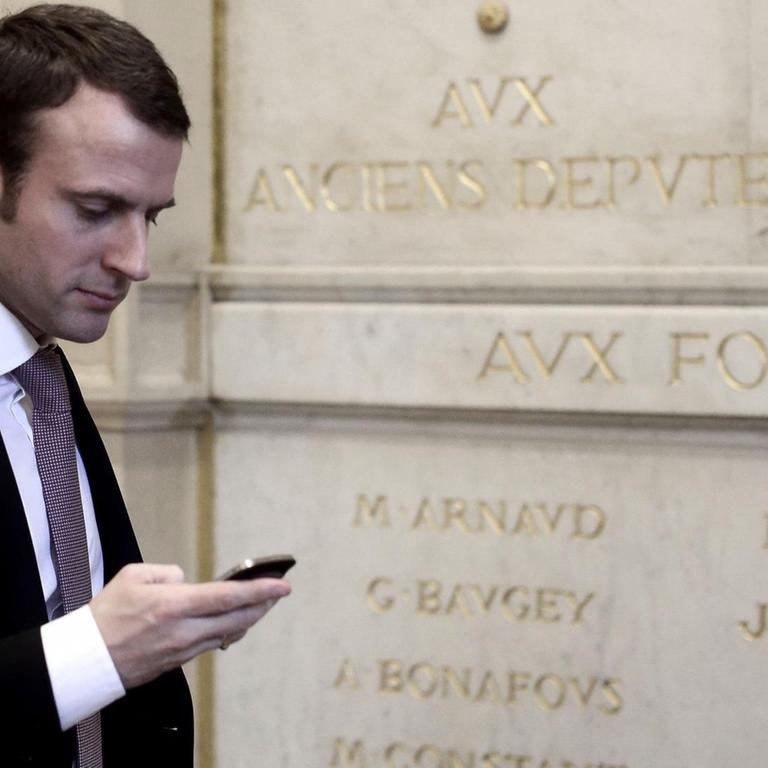 Der französische Präsident Emmanuel Macron schaut auf sein Handy