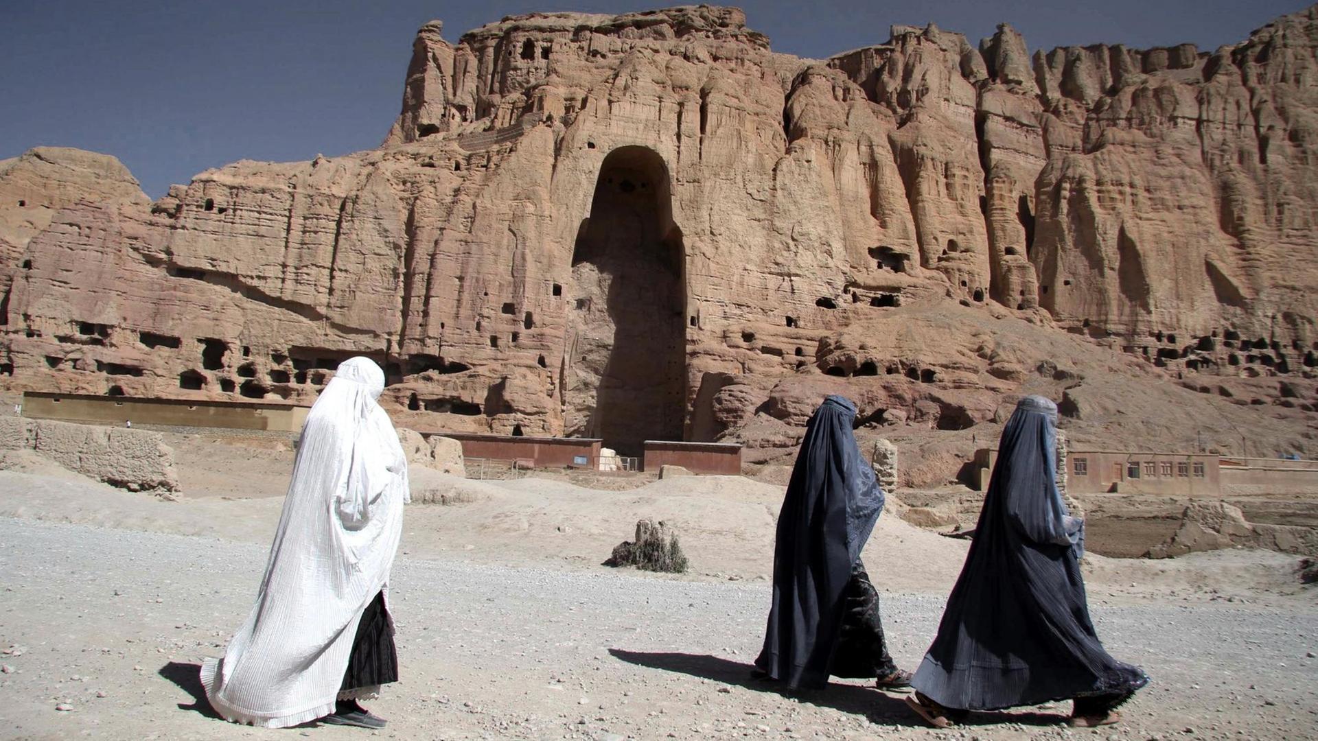 Afghanische Frauen laufen durch das Tal von Bamiyan. Im Hintergrund sieht man ein riesige Felsnische, wo die von den Taliban zerstörten Buddha-Statuen standen. Afghanische Frauen laufen durch das Tal von Bamiyan. Im Hintergrund sieht man ein riesige Felsnische, wo die von den Taliban zerstörten Buddha-Statuen standen.