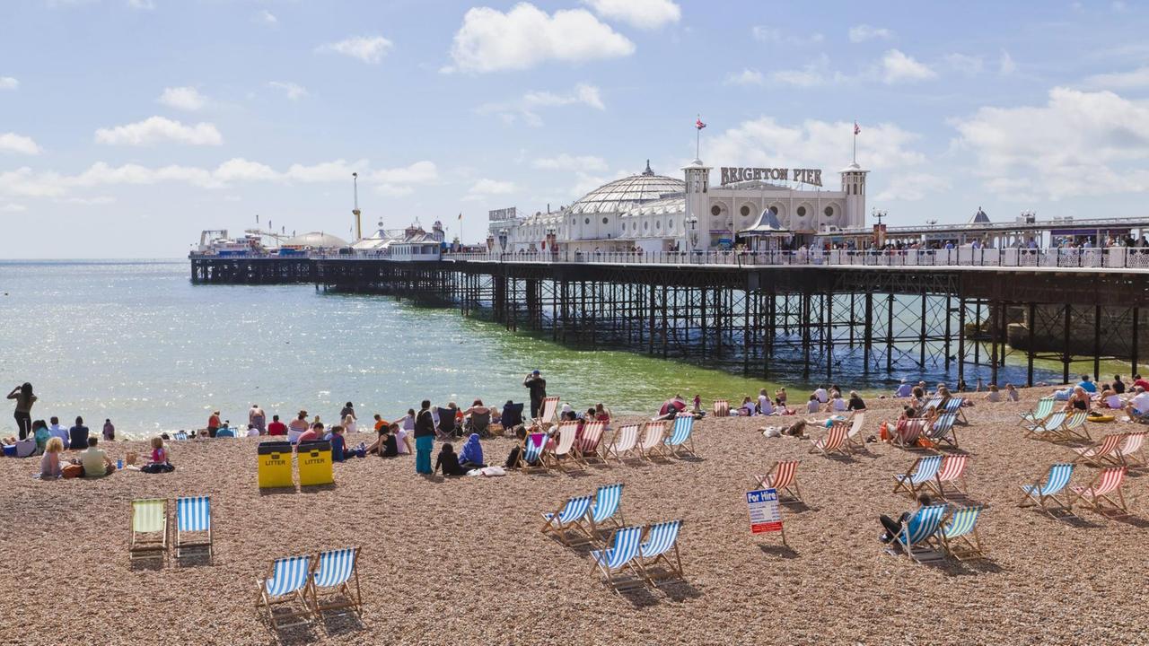 Strandliegen und Sonne bilden die Kulisse für den historischen Brighton Pier.