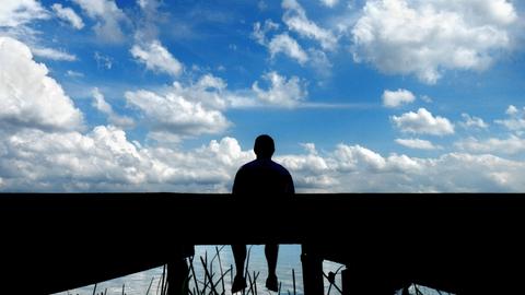 Ein Mann sitzt alleine auf einem Steg am See.