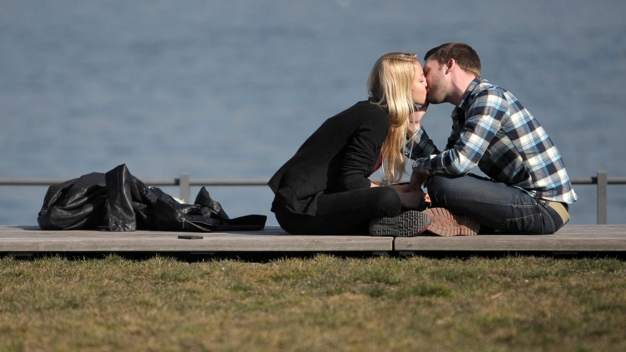 Ein verliebtes Paar genießt am Flussufer das sonnige Wetter und küsst sich auf der Uferpromenade.
