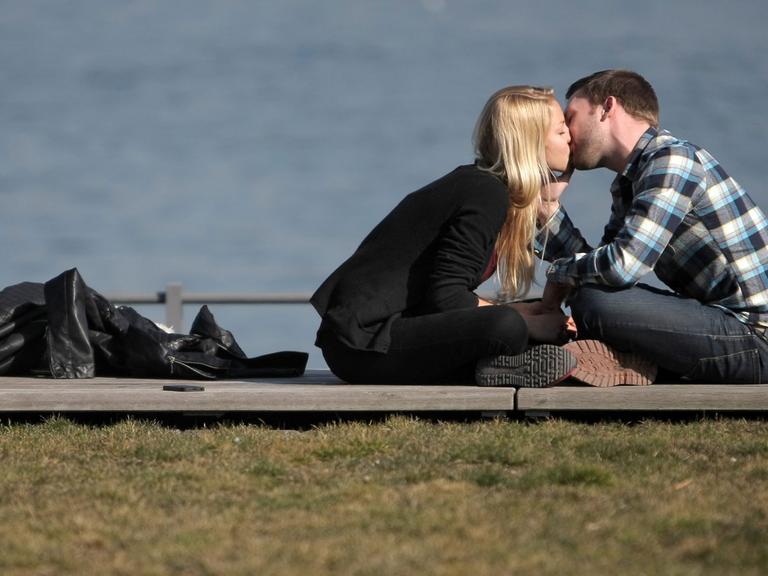 Ein verliebtes Paar genießt in Mainz am Rheinufer das sonnige Wetter und küssen sich auf der Uferpromenade.