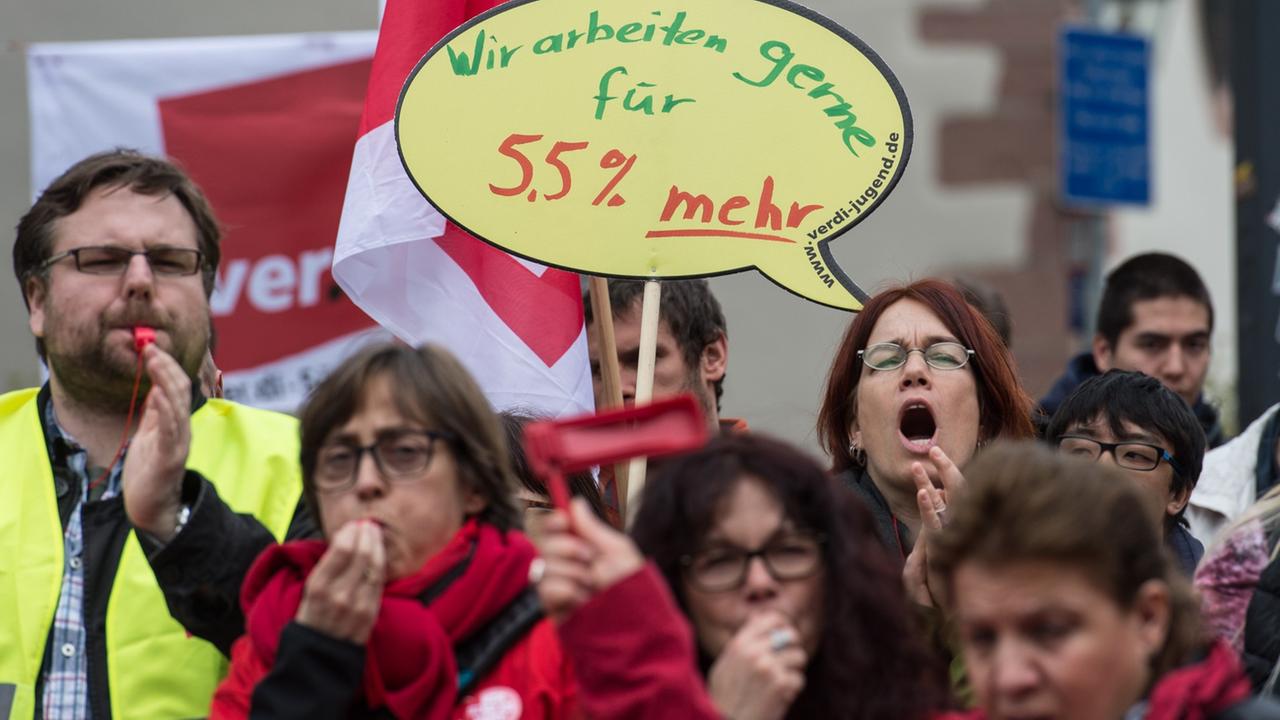 Beschäftigte der Universität Freiburg protestieren mit Trillerpfeifen und Plakaten. 