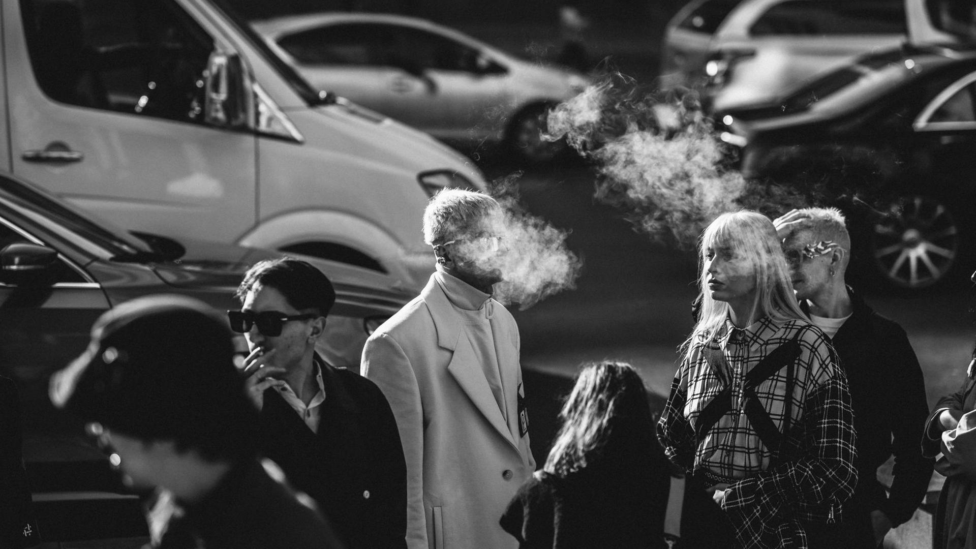 An einer Straßenkreuzung, steigt der Zigarettenqualm einiger Raucher in die Luft.