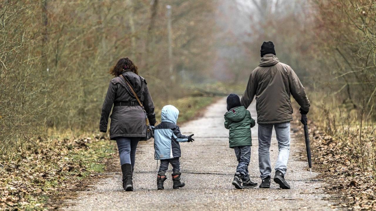 Eine Familie beim Spaziergang. Mutter und Vater laufen außen und die Kinder in der Mitte aber weit voneinander entfernt.
