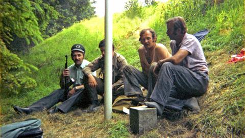 Ein bayerischer Grenzpolizist neben seinem DDR-Kollegen mit dessen Dienstmütze und Kalaschnikow. Daneben zwei ostdeutsche Bauarbeiter. Sommer 1981 an der deutsch-deutschen Grenze zwischen Hof und Plauen.