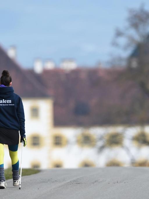 Eine Internatsschülerin läuft vor dem Schloss Salem (Baden-Württemberg) mit Walking-Stöcken einen Weg entlang.
