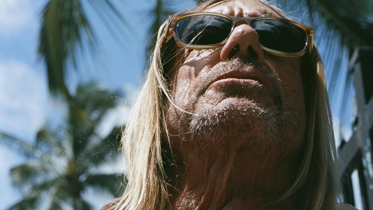 Iggy Pop sitzt mit nacktem Oberkörper genüsslich in der Sonne.