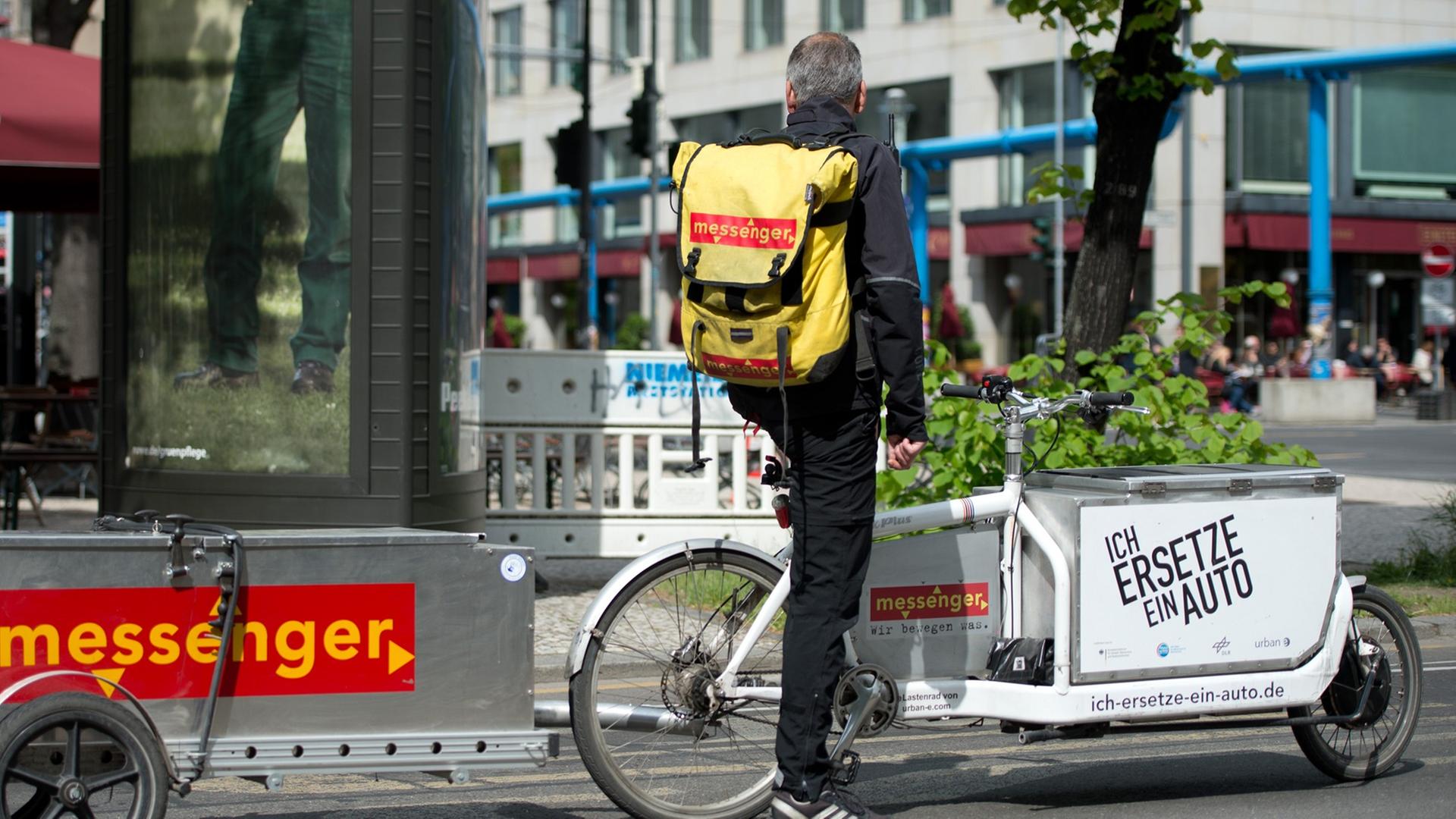 Ein Kurierfahrer mit einem Lastenfahrrad wartet in Berlin an einer Ampel auf die Weiterfahrt.