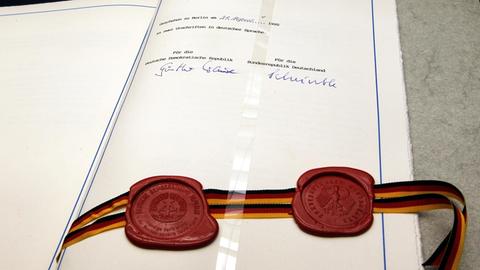 Die letzte Seite des Einigungsvertrages liegt aufgeschlagen auf einem Tisch. Zu sehen sind zwei rote Siegel, verbunden mit einem Band in schwarz-rot-gold, sowie die Unterschriften der Verhandlungsführer Günther Krause und Wolfgang Schäuble.