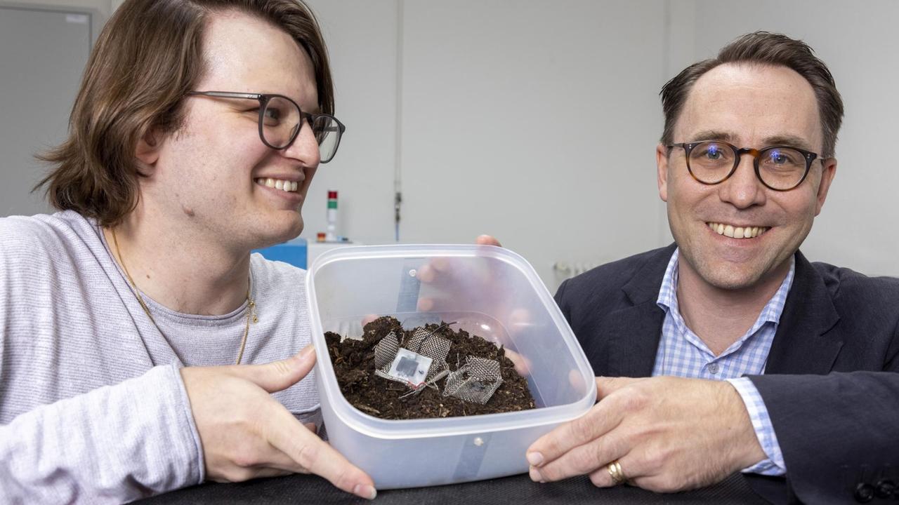 Xavier Aeby und Gustav Nyström halten einen Korb mit Erde in der Hand, im dem sie die komplett gedruckte, biologisch abbaubare Batterie präsentieren