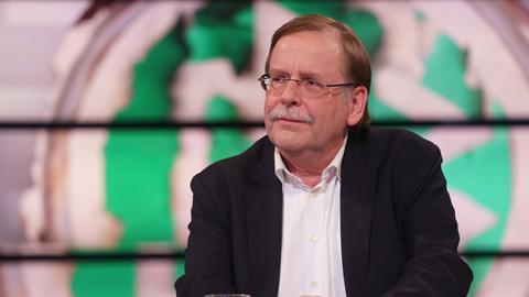 Rainer Koch sitzt vor einer Grafik eines verschwommenen DFB-Wappens.