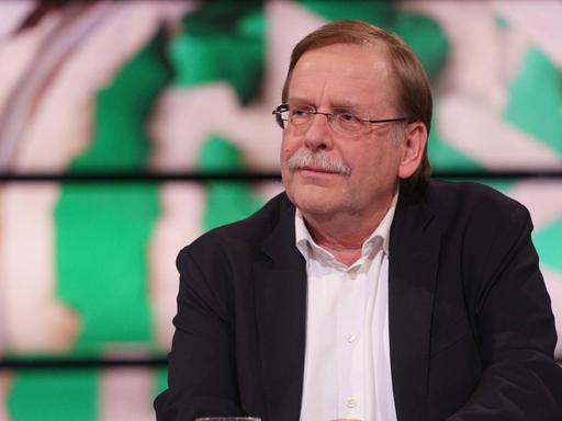 Rainer Koch sitzt vor einer Grafik eines verschwommenen DFB-Wappens.