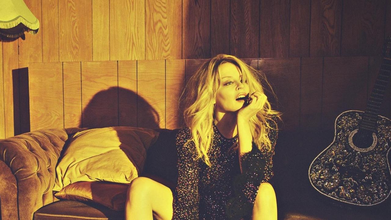 Kylie Minogue sitzt auf einem alten Sofa und rechts von liegt eine typische Country Gitarre