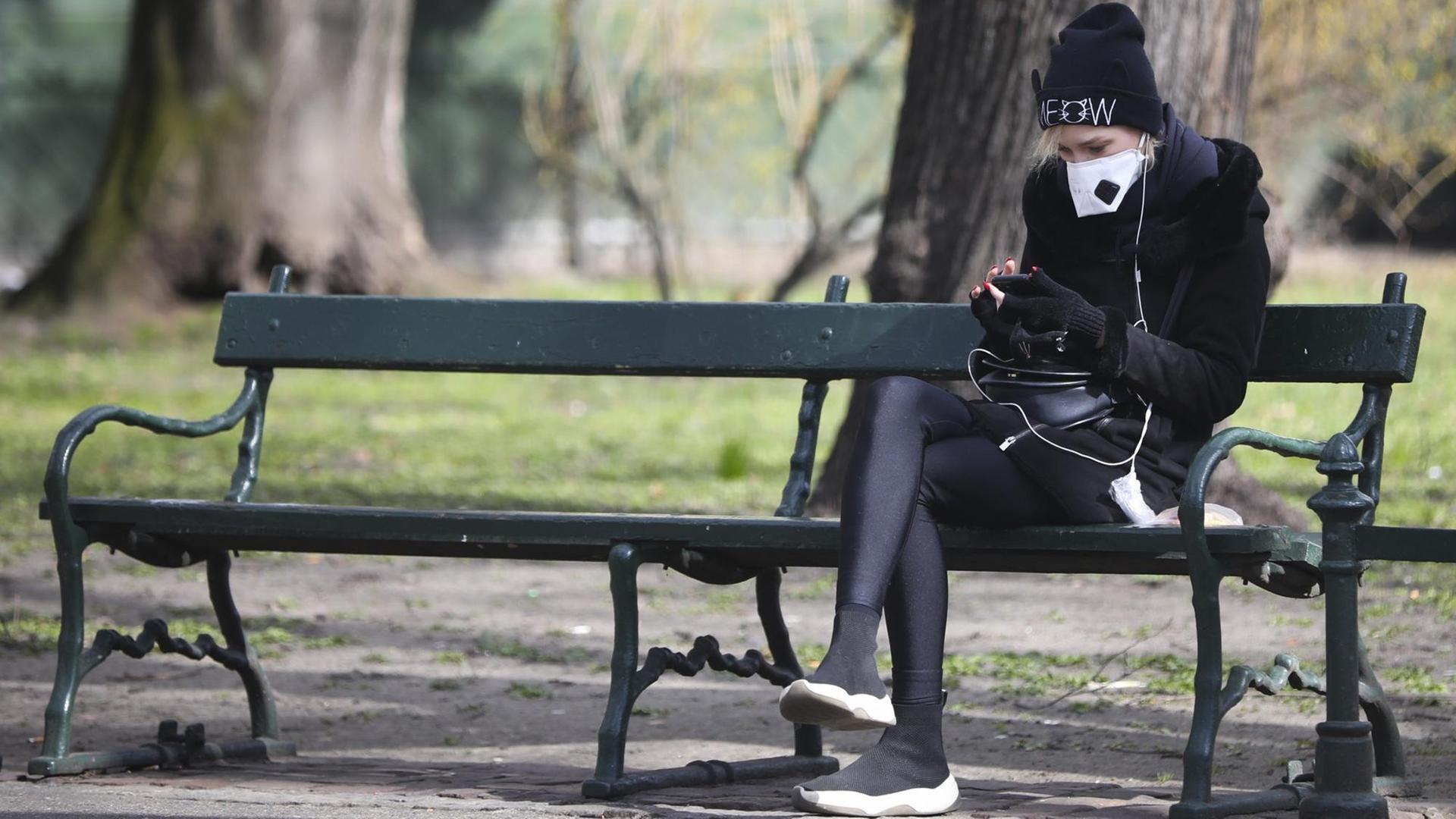 Ein Mädchen sitzt während der Corona-Krise mit einem Mundschutz allein auf einer Bank in Krakau