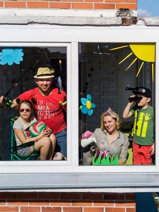 Das Foto zeigt eine Familie, die sich hinter einem Fenster ihrer Wohnung versammelt hat und sich offenbar von der Coronapandemie nicht unterkriegen lässt.