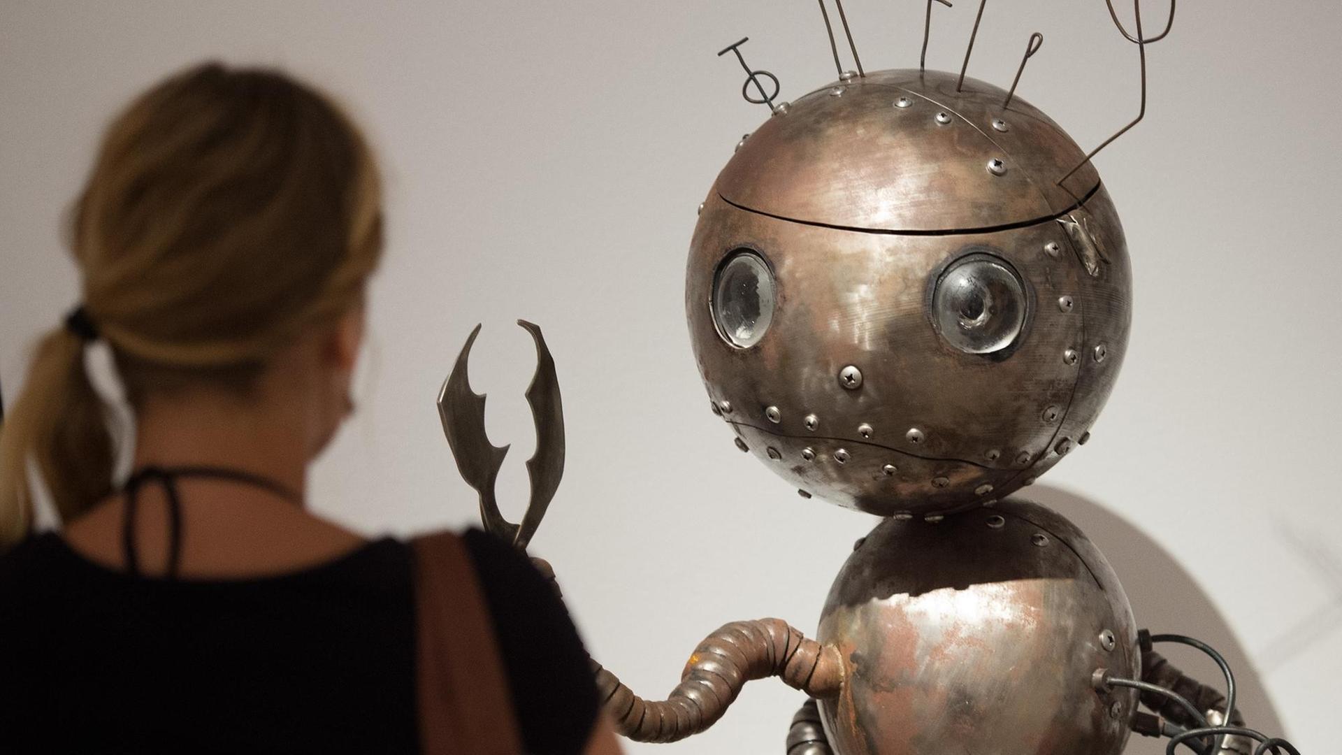 Eine Frau betrachtet die eine Metall-Figur mit rundem Kopf in der Tim-Burton-Ausstellung in Brühl.