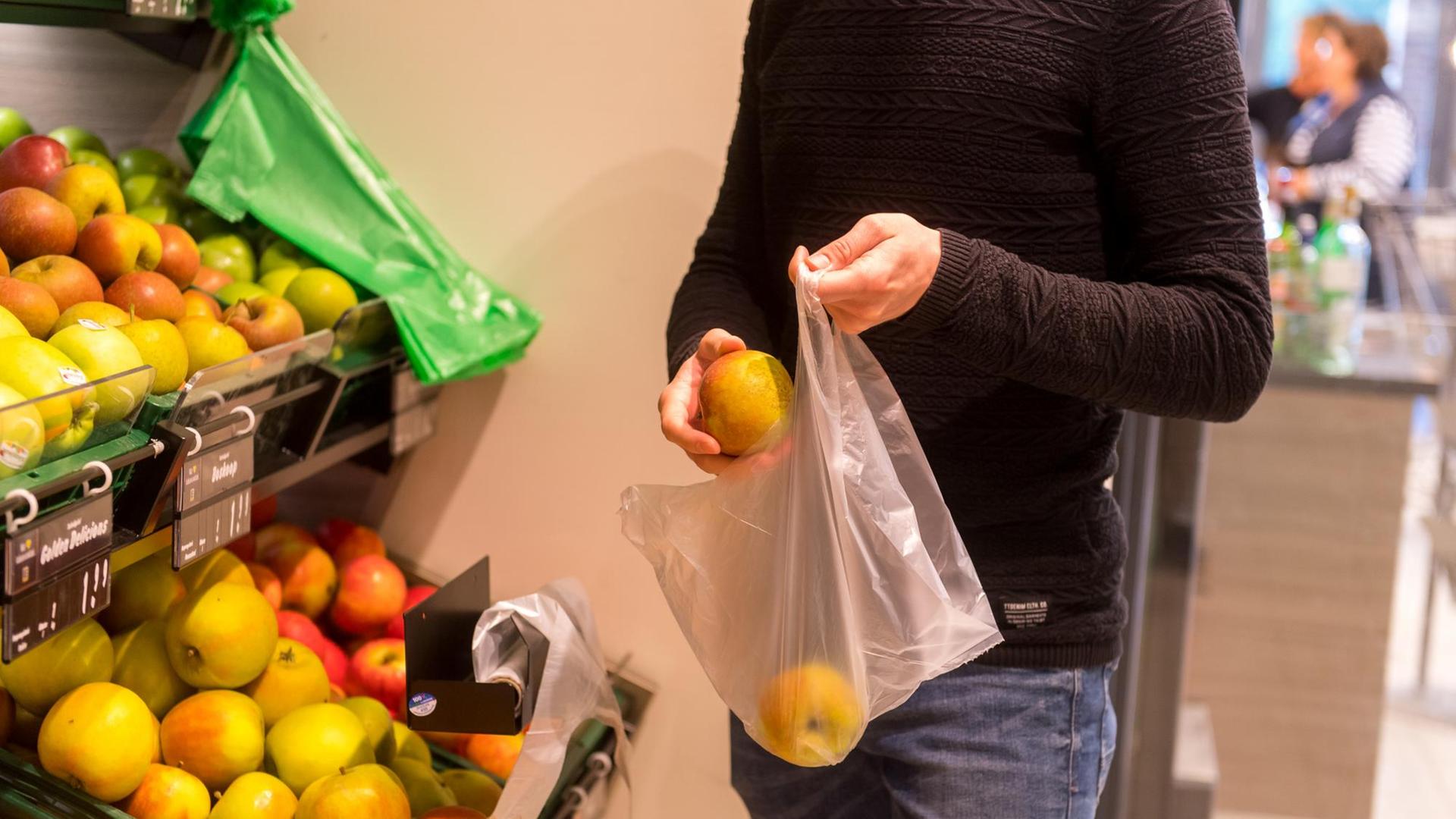 Ein Mann, dessen Kopf man nicht sieht, packt in einem Supermarkt Obst in einen Plastikbeutel.