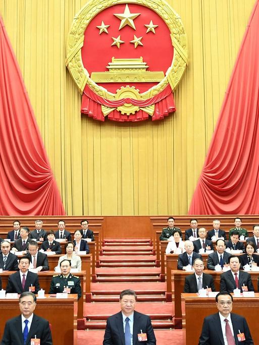 Der Nationalkongress der kommunistischen Partei Chinas in Peking im März 2019. Männer und Frauen sitzen in mehreren Reihen in einem großen Saal.