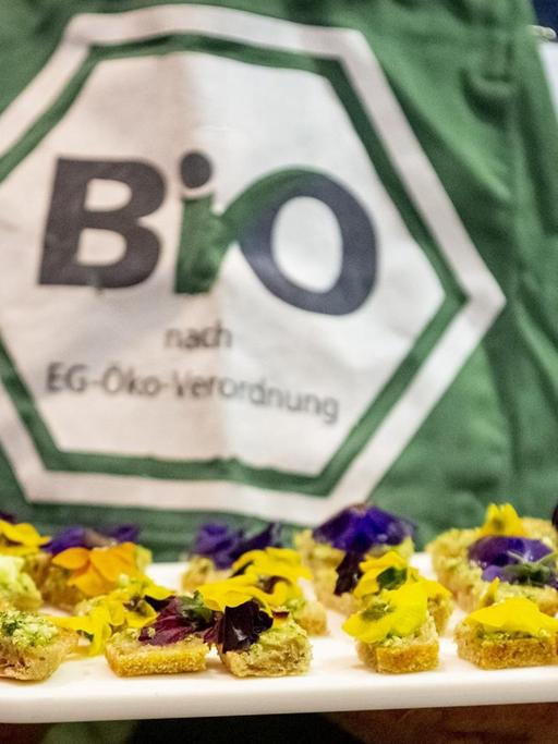 Ein Mitarbeiter hält bei der Grünen Woche in Berlin ein Brett mit Häppchen, wobei das deutsche staatliche Bio-Siegel auf seiner Schürze zu sehen ist.