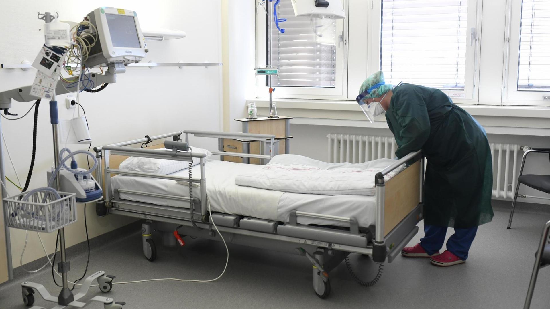 Eine Krankenpflegerin in Schutzkleidung überprüft ein leeres Bett auf der Intensivstation.